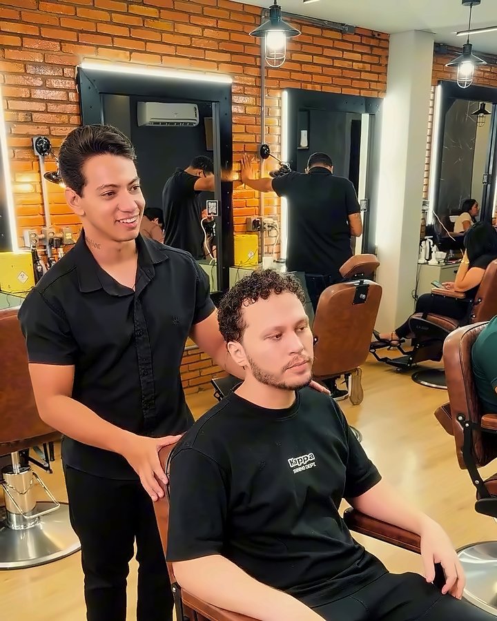 Barbeiro da Don Barbu acomodando o cliente na cadeira de couro, com a parede de tijolo ao fundo
