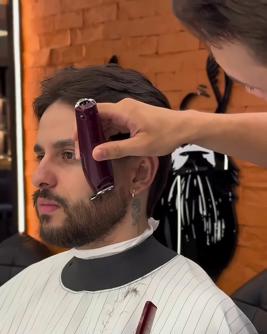 Máquina no contorno da barba diante da parede de tijolo