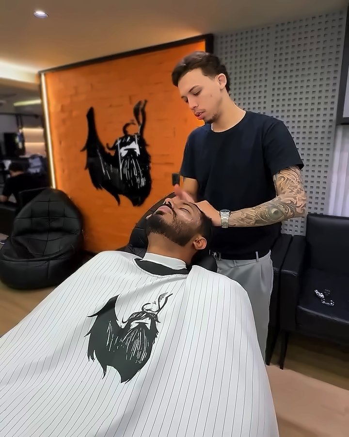 Barbeiro preparando o cliente para a toalha quente diante da parede de tijolo com a barba Don Barbu
