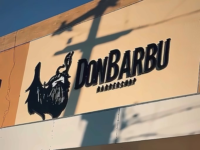 Fachada creme da Don Barbu com a barba ilustrada e o letreiro DonBarbu Barbershop